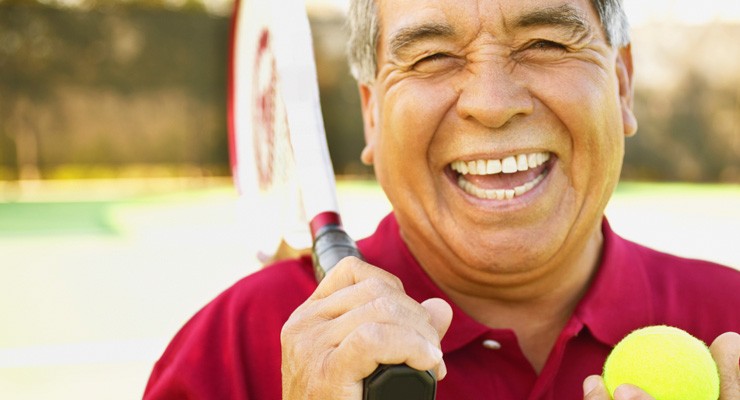 man smiling holding a tennis racket and tennis ball