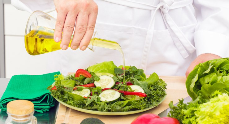 person pouring olive oil on plate of salad